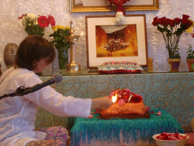 Photo of Navya waving a camphor flame in front of Amma's silver padukas that are covered with rose petals after a pada puja.